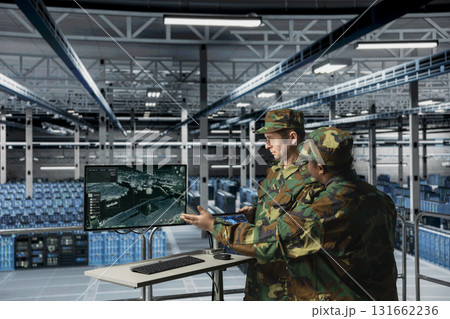 Teamworking army experts in data center visualizing thermal surveillance feed from deployed satellites. Military units in server room tracking enemy hostile movements using orbital scans 131662236