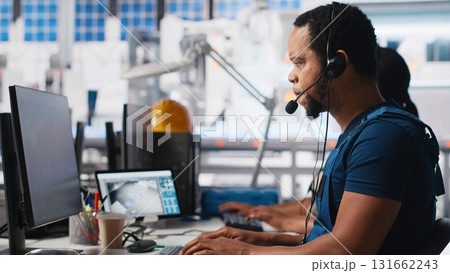 Call center technician handling maintenance inquiries in solar factory, working in customer service industrial tech support. African american operator on headset with clients. Camera A. 131662243