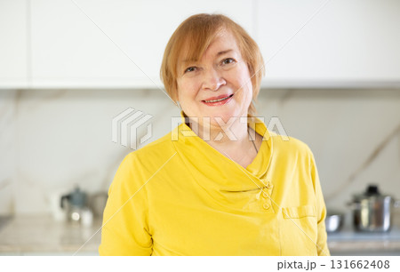 Happy mature woman cooking in her kitchen with radiant smile 131662408
