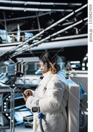 Female astronaut preparing for scientific mission, operating spacecraft control interface using tablet. Spaceship crew member in spacesuit looking at planetary exploration data on device screen 131662409