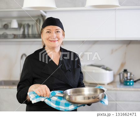 Adult woman in cook uniform posing with frying pan Adult woman in cook uniform posing with frying pan 131662471