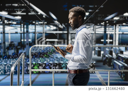 Young data center male employee on platform works on neural network software tasks. Confident african american engineer visualizing large language model architecture, technical support. 131662480