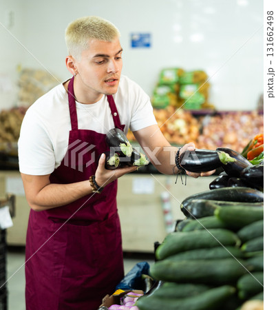 Grocery store employee places ripe eggplants on a display case at street store 131662498