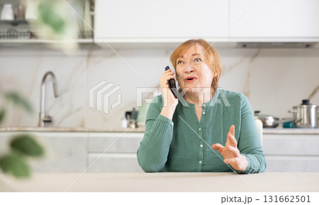 Adult woman talking on mobile phone in kitchen 131662501