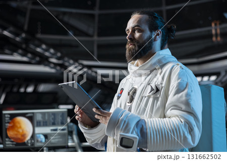 Cosmonaut checking starship diagnostics on device before Mars expedition, preparing for future of mankind. Astronaut in orbital station explores red planet to support human life beyond Earth 131662502