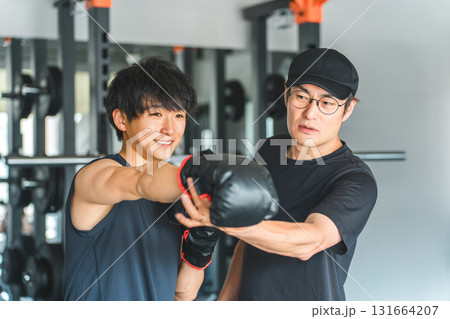 ジム,トレーニングジムでボクササイズをする若いアジア人男性とトレーナーの男性スタッフ ジム,トレーニングジムでボクササイズをする若いアジア人男性とトレーナーの男性スタッフ 131664207