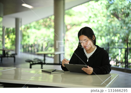 Focused high school student studying with digital tablet and stylus at school campus 131666295