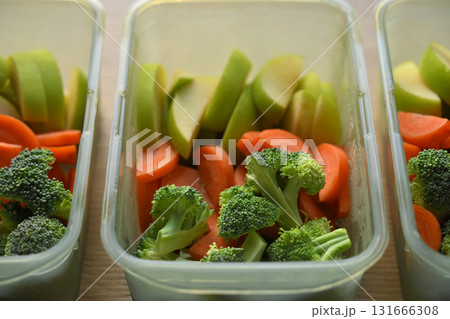 Healthy weekly meal prep with fresh broccoli, sliced carrots, and green apples neatly arranged in food containers 131666308