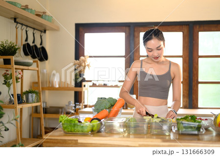 Smiling woman doing weekly meal prep with fresh produce on wooden table in a modern kitchen 131666309