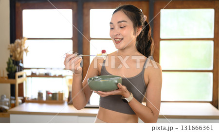 Young woman in sportswear eating a yogurt bowl with berries. Clean eating and healthy lifestyle concept. 131666361