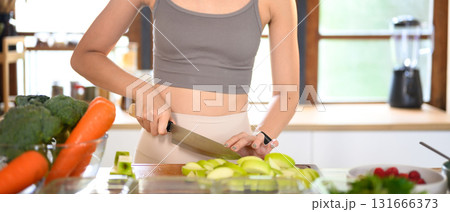 Young woman slicing green apples on a cutting board surrounded by fresh fruits and vegetables. Concept of weekly meal prep Young woman slicing green apples on a cutting board surrounded by fresh fruits and vegetables. Concept of weekly meal prep 131666373