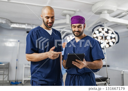 Two surgeons in scrubs discuss a patient's medical records in a modern operating room, illuminated by surgical lights. 131667179