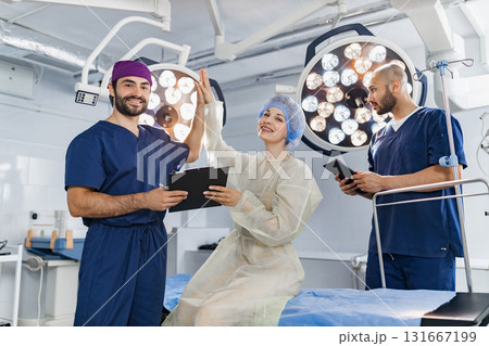 Medical professionals celebrate a successful procedure in a modern operating room, high-fiving and smiling. Medical professionals celebrate a successful procedure in a modern operating room, high-fiving and smiling. 131667199