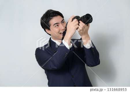 白背景でカメラを構えるスーツの男性 131668953