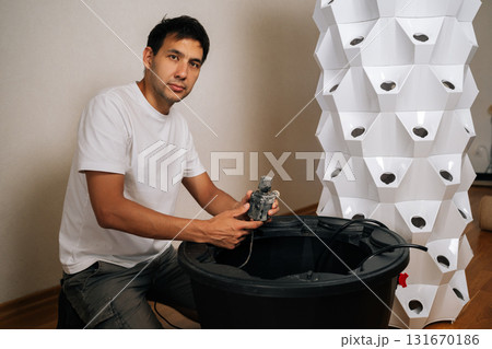 Home gardener installing water pump in reservoir of aeroponic vertical farming system, cultivating plants without soil in innovative and sustainable way at home. Concept of urban farming. 131670186