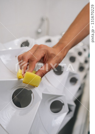 Vertical shot of gardener male cleaning vertical hydroponic tower garden with yellow sponge in modern bathroom, ensuring cleanliness and optimal growing conditions. Concept of home gardening. 131670229