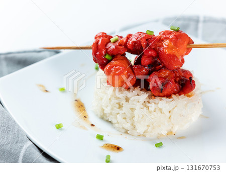 Seasoned red chicken skewers served on a small mound of white steamed sticky rice on a square white plate. Asian or fusion cuisine. Seasoned red chicken skewers served on a small mound of white steamed sticky rice on a square white plate. Asian or fusion cuisine. 131670753