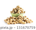 A light green bowl overflowing with roasted peanuts in the shell, isolated on a clean white background. Healthy snack or ingredient. 131670759
