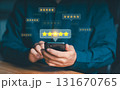 Hand holding a phone displaying multiple floating 5-star rating icons. Concept of customer satisfaction, quality feedback, and online reviews. 131670765