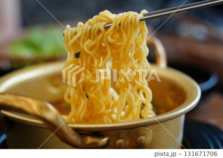 Spicy Korean instant ramen noodles in a traditional pot, lifted with chopsticks. 131671706