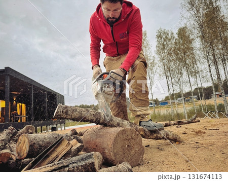 A man cutting a log into firewood using a chainsaw 131674113