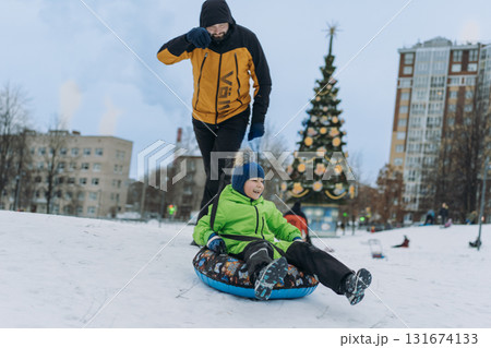 father and boy sliding down the slope in park . Winter family activities concept.  131674133