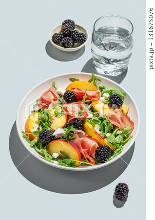 Salad with peaches, arugula, feta, prosciutto and berries in a plate on a blue background 131675076