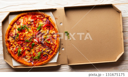 Pepperoni pizza with bell peppers sweetcorn and arugula in open carton box on white wooden kitchen table flat lay view. Copy-space 131675175