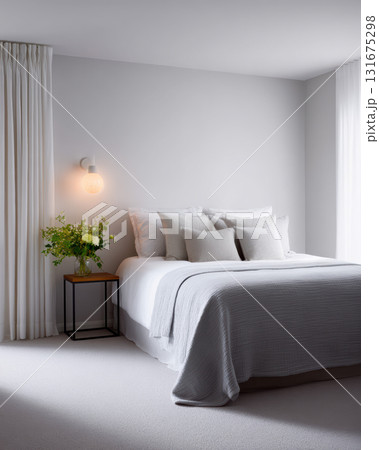Calm and serene minimalist bedroom interior with comfortable bed, soft pillows, and cozy grey blanket. warm lamp provides soft light next to elegant white curtain 131675298