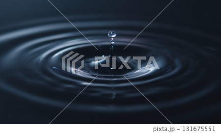 Single calm drop of dark water liquid creates splash and ripple upon impact with surface. resulting circle pattern expresses tranquility and peaceful moment Single calm drop of dark water liquid creates splash and ripple upon impact with surface. resulting circle pattern expresses tranquility and peaceful moment 131675551