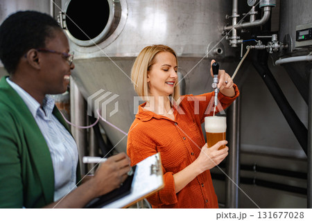 Women pouring beer during quality control inspection in brewery 131677028
