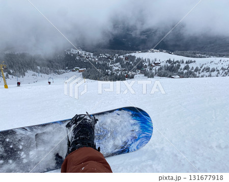 Snowboarder on Slope Overlooking Ski Resort 131677918