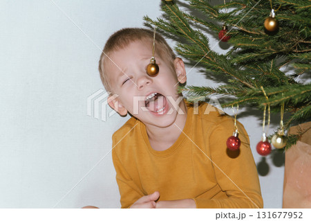 Festive baby boy in yellow sweater getting ready to decorate the Christmas tree, creating a warm holiday atmosphere for celebrating with loving family members tonight. 131677952