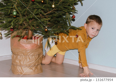 Festive baby boy in yellow sweater getting ready to decorate the Christmas tree, creating a warm holiday atmosphere for celebrating with loving family members tonight. Festive baby boy in yellow sweater getting ready to decorate the Christmas tree, creating a warm holiday atmosphere for celebrating with loving family members tonight. 131677954