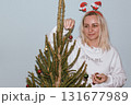 Beautiful young woman wearing knitted sweater and woolen hat standing near red car with Christmas tree on the top under snowfall. Happy winter holidays 131677989