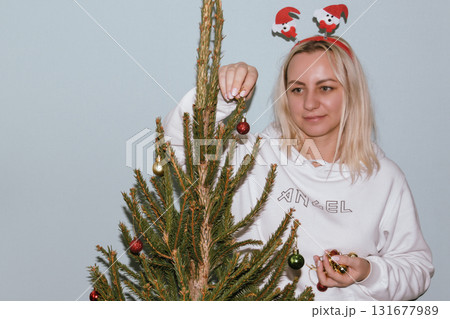 Beautiful young woman wearing knitted sweater and woolen hat standing near red car with Christmas tree on the top under snowfall. Happy winter holidays Beautiful young woman wearing knitted sweater and woolen hat standing near red car with Christmas tree on the top under snowfall. Happy winter holidays 131677989