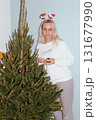 Beautiful young woman wearing knitted sweater and woolen hat standing near red car with Christmas tree on the top under snowfall. Happy winter holidays 131677990
