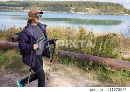 Woman hiking near lake with trekking poles on sunny day Woman hiking near lake with trekking poles on sunny day 131678085