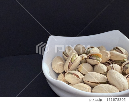Pistachios in a white bowl. Bowl of pistachios on dark background. Pistachios in a white bowl. Bowl of pistachios on dark background. 131678295