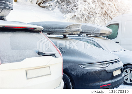 Back view of modern electric car with rooftop box covered frosty snow hoarfrost at alpine street outdoor parking oh cold winter day. Snow-covered SUV roof box parked outdoors in winter conditions Back view of modern electric car with rooftop box covered frosty snow hoarfrost at alpine street outdoor parking oh cold winter day. Snow-covered SUV roof box parked outdoors in winter conditions 131678310