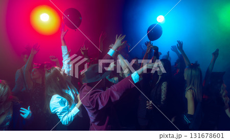 People reaching for black balloons at neon Halloween dance floor 131678601