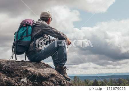 Tourist with backpack sits on the top of the mountain,resting and admiring the view from above.Active recreation concept 131679023