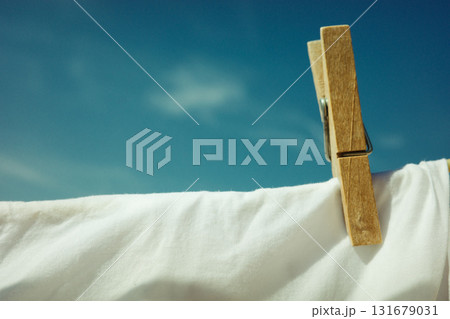 Wooden clothespin holding white fabric against blue sky Wooden clothespin holding white fabric against blue sky 131679031