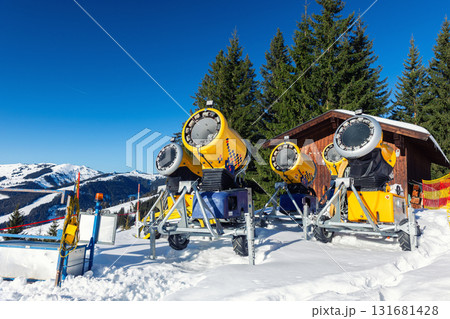 Operating artificial snow cannon near piste making snowy powder.Ski lift ropeway on hilghland alpine mountain winter resort on bright sunny day. downhill slopes with people enjoy sport activities 131681428