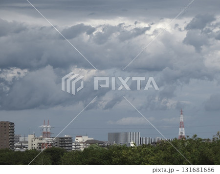 分厚い積乱雲が空を覆い、都市の風景と送電鉄塔を飲み込む不穏な空模様 131681686