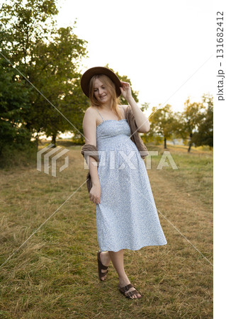 Pregnant woman walking outdoors in summer dress at sunset Pregnant woman walking outdoors in summer dress at sunset 131682412