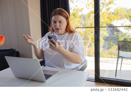 Frustrated woman arguing on smartphone while working on laptop at home Frustrated woman arguing on smartphone while working on laptop at home 131682442