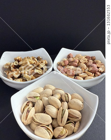 Bowls of pistachios, walnuts, and peanuts  on dark background. Assorted nuts in bowls. 131682553
