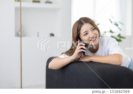 ソファーに座ってスマートフォンで通話をする若い女性 131682569