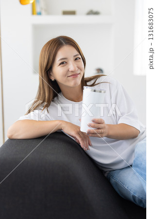 タンブラーを手にソファに座る若い女性 131683075